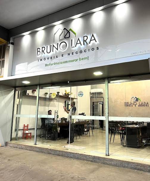 Loja da Bruno Lara Imóveis à noite, com letreiro Referência em morar bem e equipe trabalhando atrás da vitrine